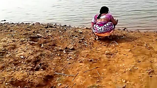 Indian woman peeing in the dirt by a lake